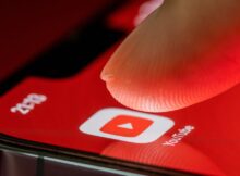 Finger touches the Youtube application on smartphone screen on red background